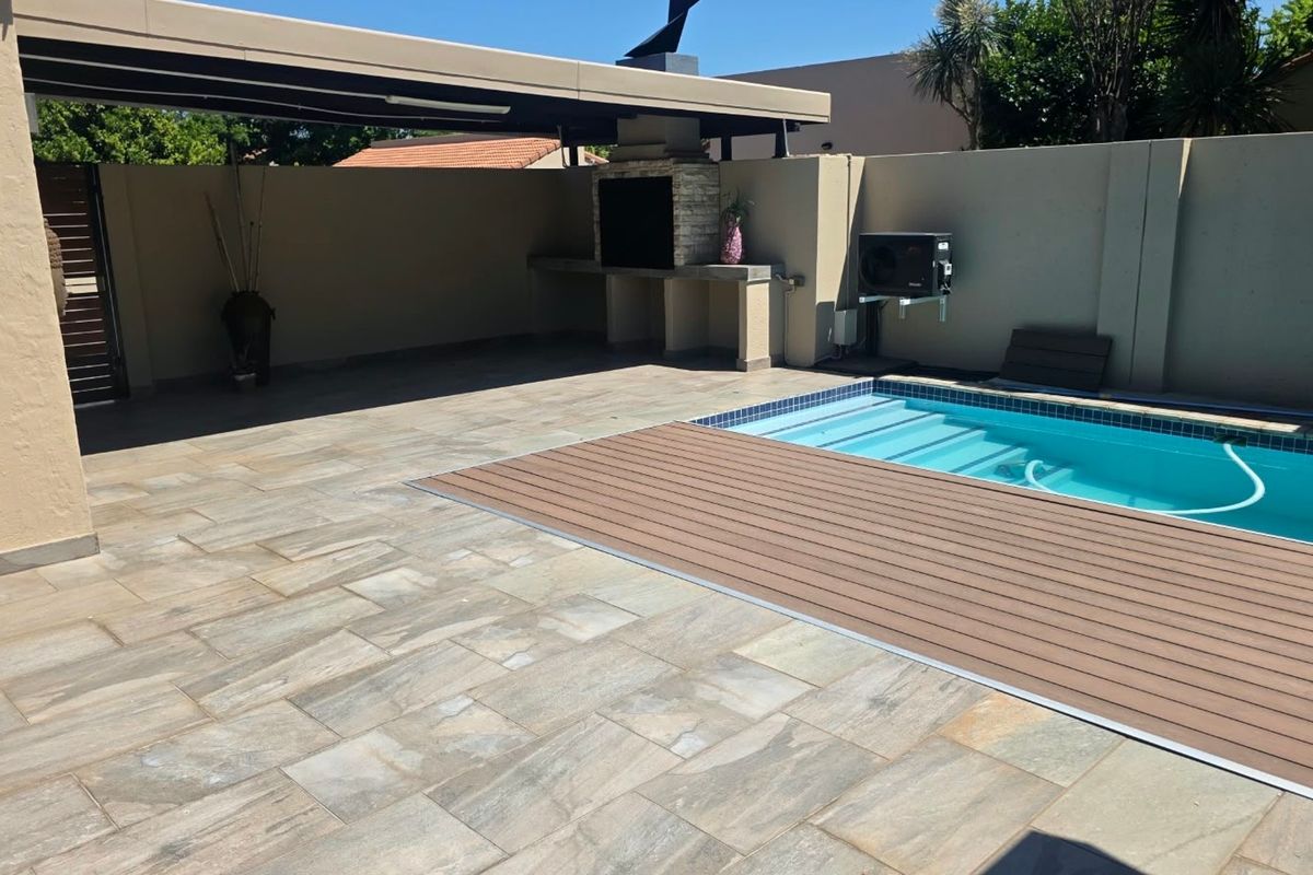 Outdoor entertainment area featuring a swimming pool with composite decking, a covered patio, and a built-in braai, set within a private walled garden.