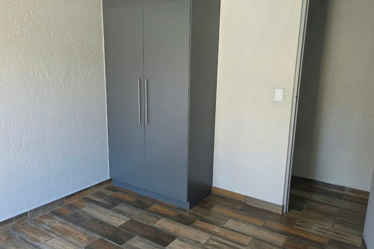 A clean, empty bedroom featuring modern grey built-in cupboards and wood-look tiled flooring.