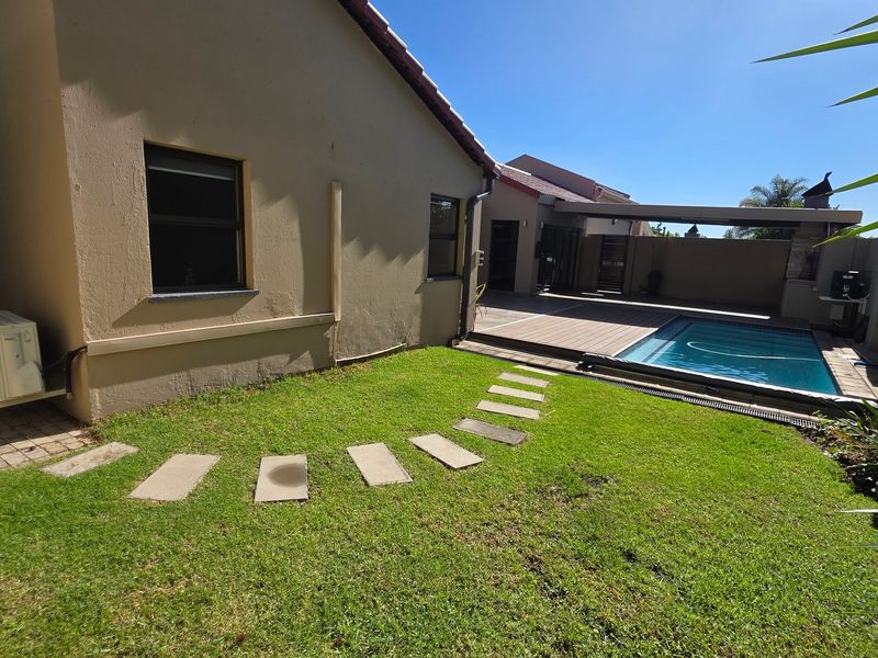 A well-maintained rear garden featuring a swimming pool, wooden decking, and a paved pathway, set against the side elevation of the cluster home.