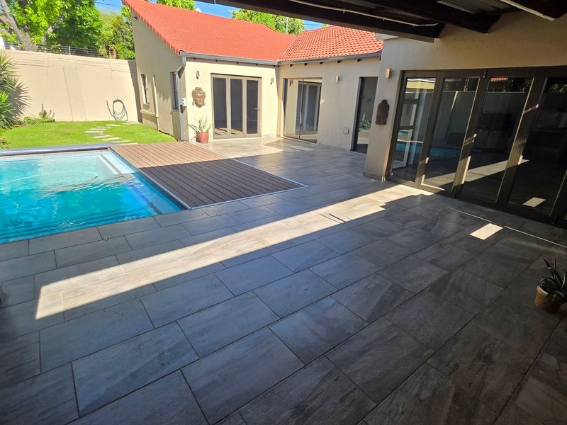 A well-maintained outdoor entertainment area featuring a swimming pool with a composite deck, tiled patio flooring, and direct access to the home via sliding doors.