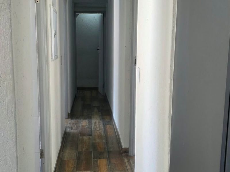 A narrow interior hallway featuring wood-look tile flooring and neutral wall finishes, providing access to multiple rooms within the property.