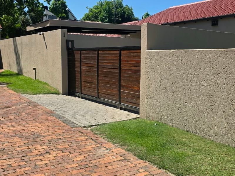 Front view of the property featuring a brick driveway, secure sliding wooden gate, and perimeter walling with an integrated carport.
