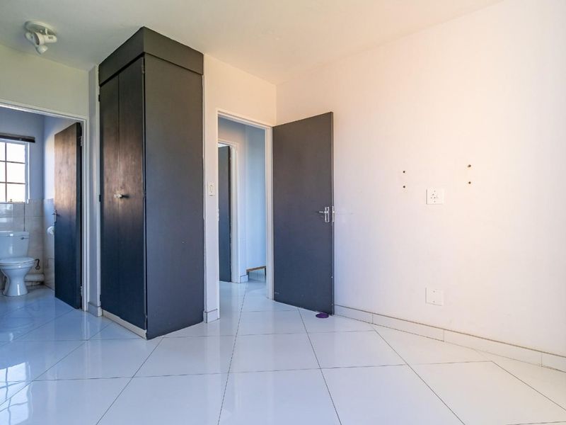 An empty bedroom featuring tiled flooring, a built-in cupboard, and direct access to an en-suite bathroom.
