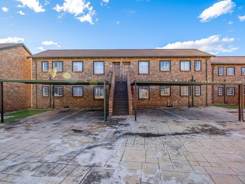Front elevation of a two-story face brick townhouse complex featuring covered carports, paved driveway, and external staircase access to upper units.