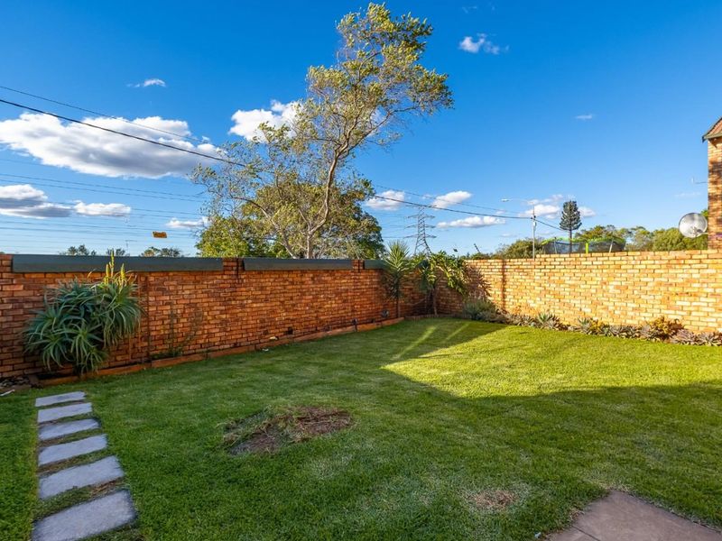 A private rear garden featuring a well-maintained lawn, paved walkway, and secure brick boundary wall with electric fencing.
