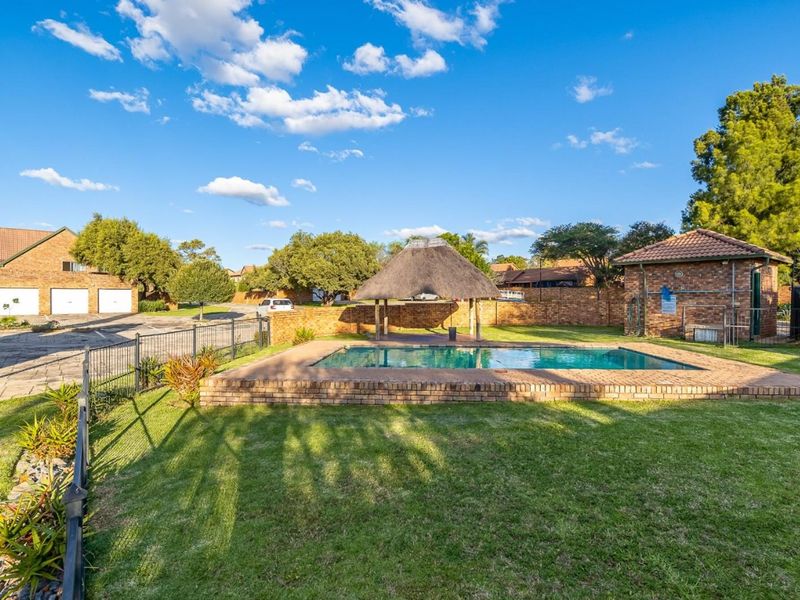 Communal outdoor area featuring a swimming pool, a traditional thatch lapa, and well-maintained lawn, set within a secure brick-walled complex.