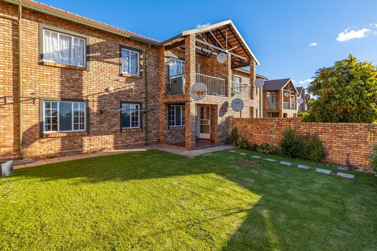 Rear view of a face brick townhouse featuring a private garden, a covered balcony with metal railings, and a secure brick boundary wall.