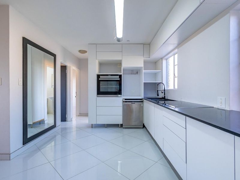 Modern kitchen featuring sleek white cabinetry, black stone countertops, integrated dishwasher, built-in oven, and polished tiled flooring in a bright, open layout.