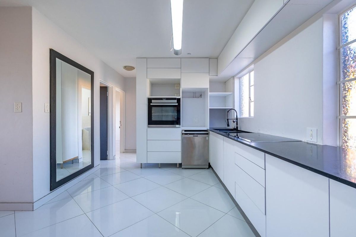 Modern kitchen featuring sleek white cabinetry, black stone countertops, integrated dishwasher, built-in oven, and polished tiled flooring in a bright, open layout.