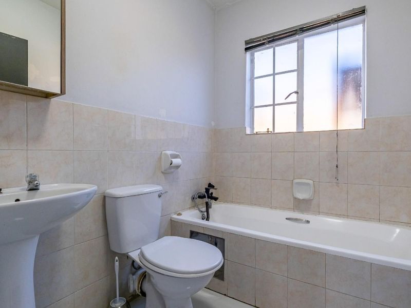 A functional bathroom featuring a pedestal basin, toilet, and bathtub with tiled walls and a window for natural light.