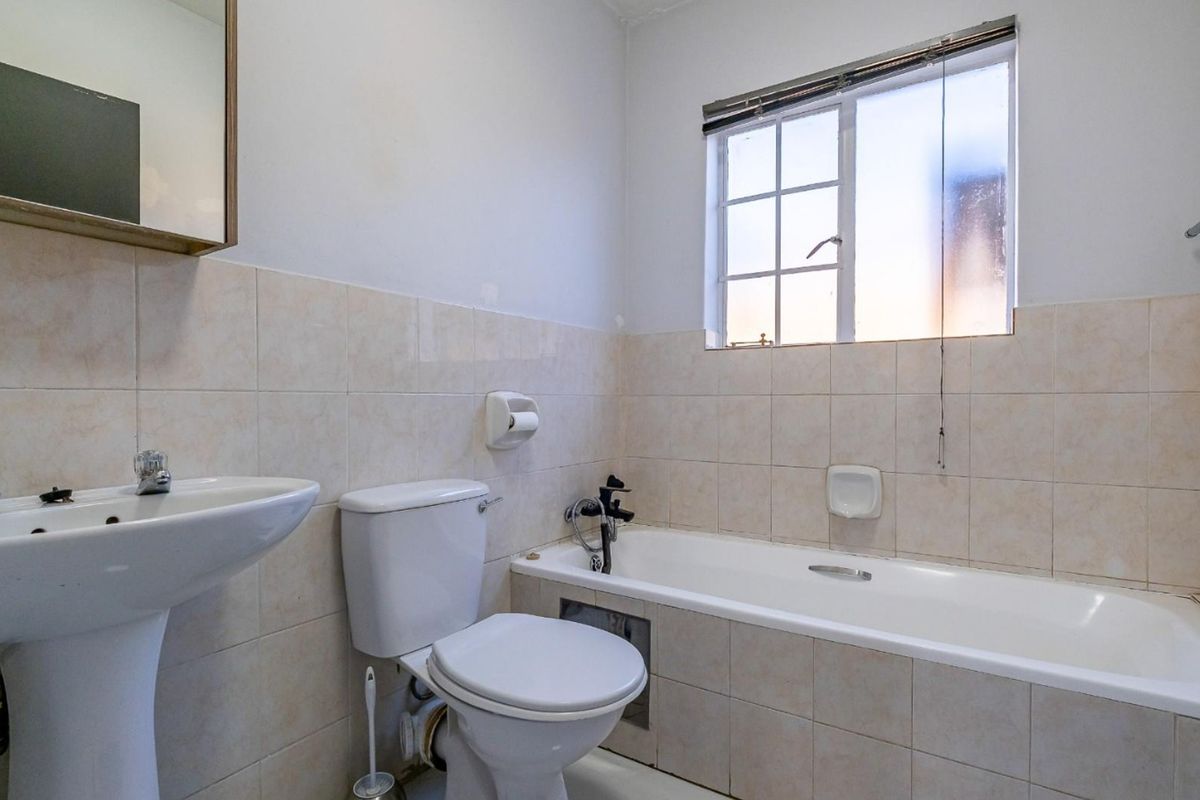 A functional bathroom featuring a pedestal basin, toilet, and bathtub with tiled walls and a window for natural light.