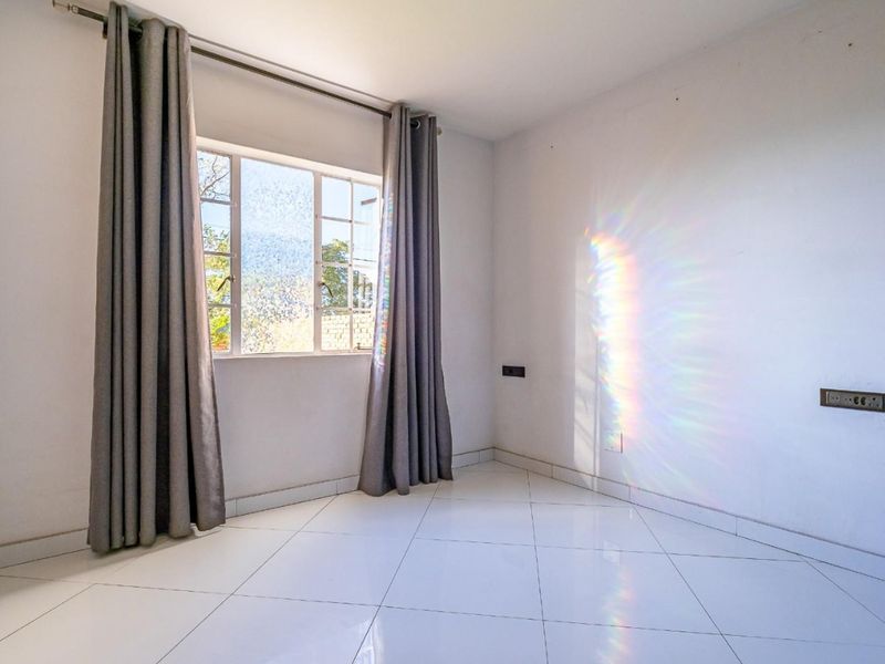 A bright, empty bedroom featuring clean tiled flooring, a window with security bars, and neutral wall finishes, ready for personalization.