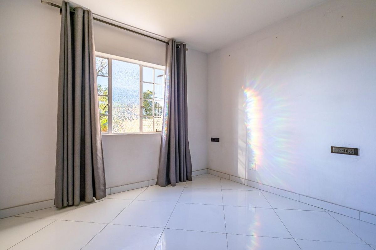 A bright, empty bedroom featuring clean tiled flooring, a window with security bars, and neutral wall finishes, ready for personalization.
