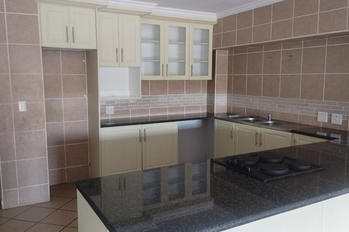 A clean, empty kitchen featuring built-in cabinetry, granite countertops, a fitted hob, and tiled finishes throughout.