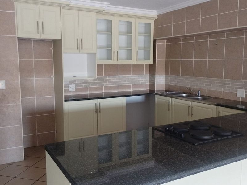 A clean, empty kitchen featuring built-in cabinetry, granite countertops, a fitted hob, and tiled finishes throughout.