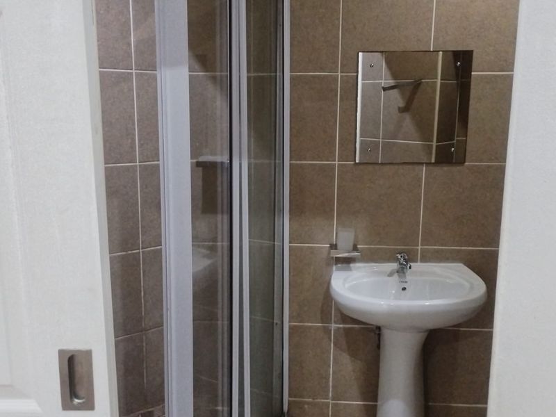 A compact bathroom featuring a pedestal basin, shower enclosure, and tiled wall finishes.