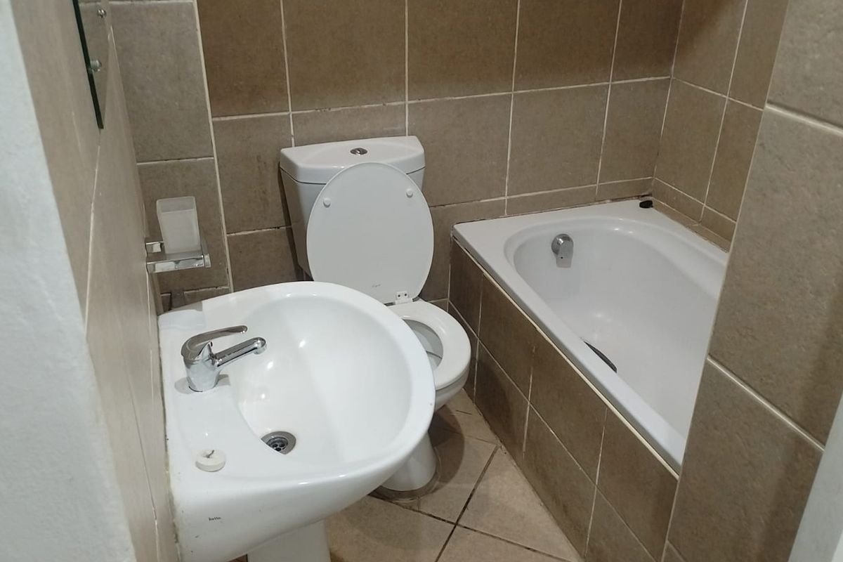 A compact bathroom featuring a pedestal washbasin, toilet, and a built-in bathtub with neutral ceramic wall and floor tiling.