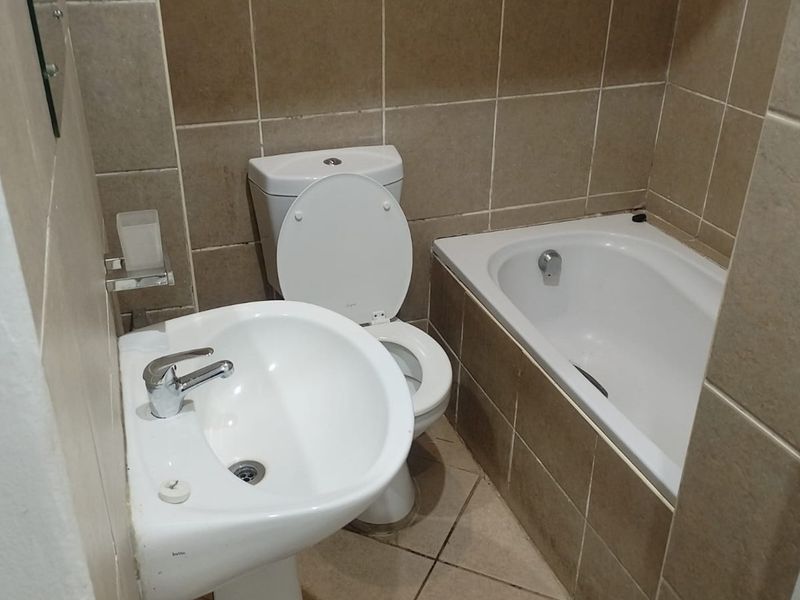 A compact bathroom featuring a pedestal washbasin, toilet, and a built-in bathtub with neutral ceramic wall and floor tiling.