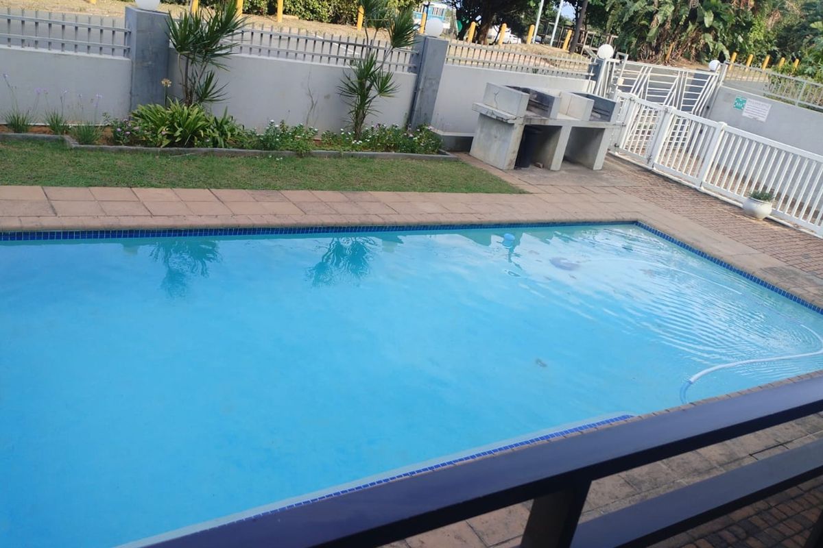 A well-maintained outdoor pool area featuring a swimming pool, paved surround, and a built-in braai facility, enclosed by a secure boundary wall.
