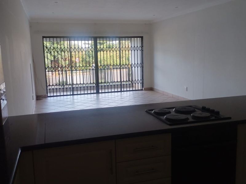 Open plan living area featuring a kitchen with built-in cabinetry and electric hob, leading to a tiled space with security gate access.