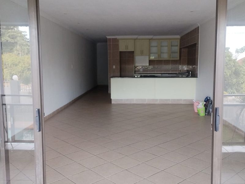 An open-plan living and kitchen area featuring tiled flooring, neutral cabinetry, and large sliding glass doors leading to an outdoor space.