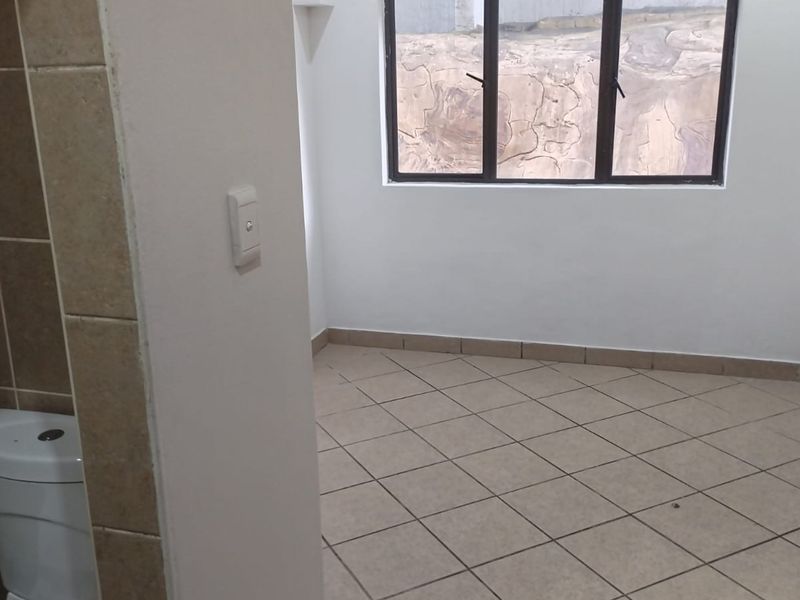 An empty bedroom featuring tiled flooring and an adjacent toilet area with an aluminium window frame.