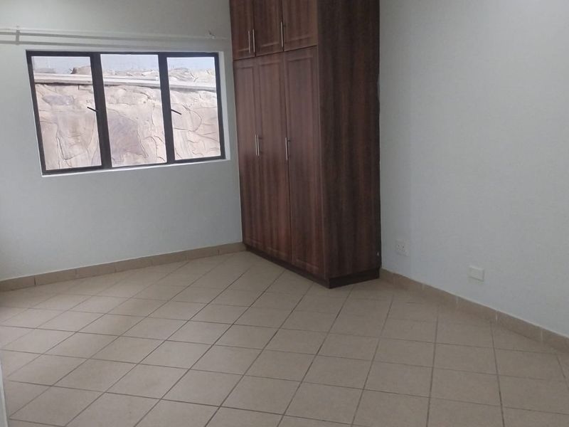 A clean, empty bedroom featuring neutral tiled flooring, a built-in wooden wardrobe, and a window with an exterior view.