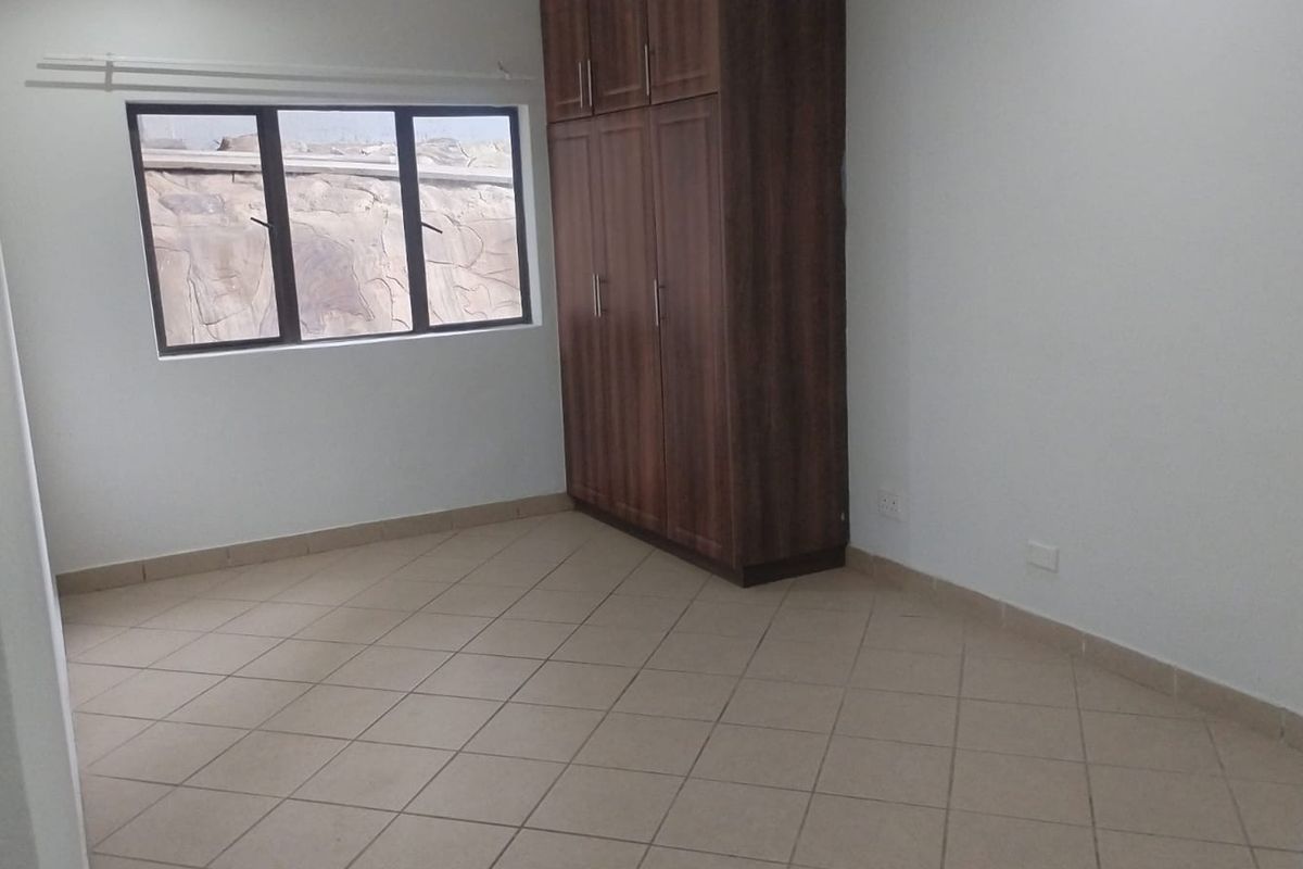 A clean, empty bedroom featuring neutral tiled flooring, a built-in wooden wardrobe, and a window with an exterior view.