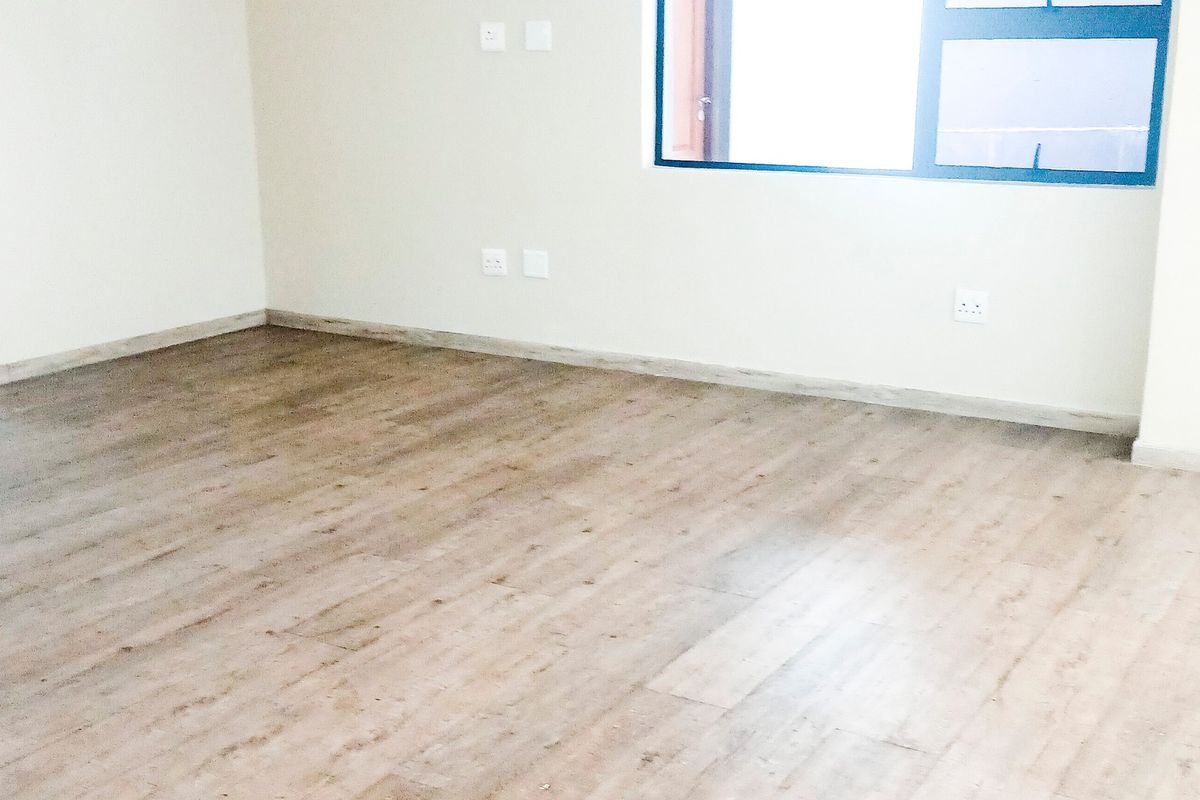 A bright, empty office space featuring modern laminate flooring, neutral walls, and an aluminium-framed window, providing a clean canvas for a professional workspace.
