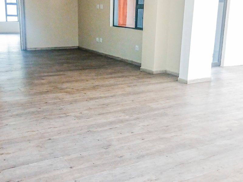A bright, open-plan office space featuring modern laminate wood flooring, neutral walls, and aluminium-framed windows, providing a clean and versatile professional environment.