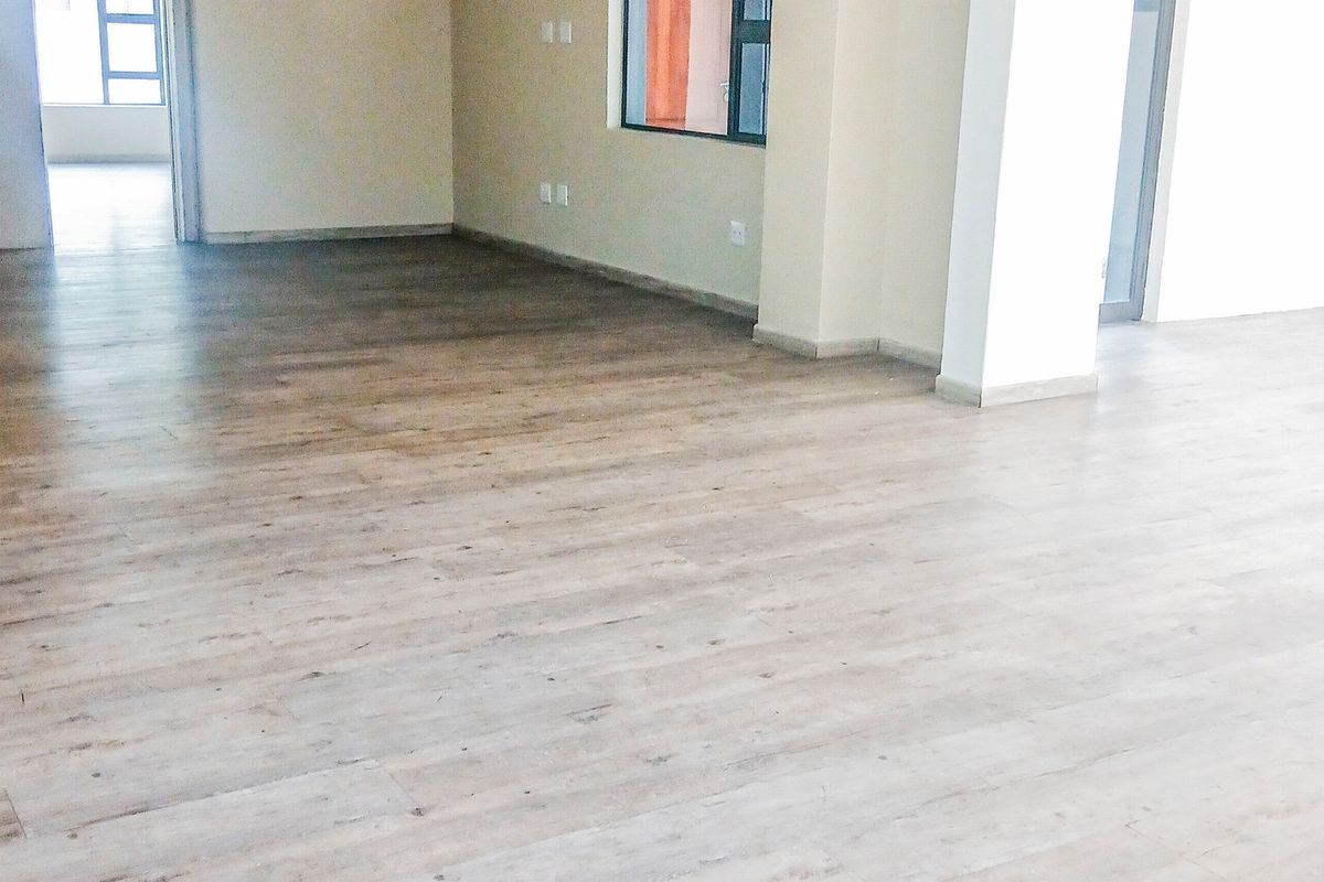 A bright, open-plan office space featuring modern laminate wood flooring, neutral walls, and aluminium-framed windows, providing a clean and versatile professional environment.
