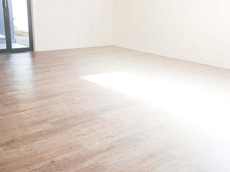 A bright, empty office space featuring modern wood-look tile flooring and a glass-paneled door leading to an outdoor area.