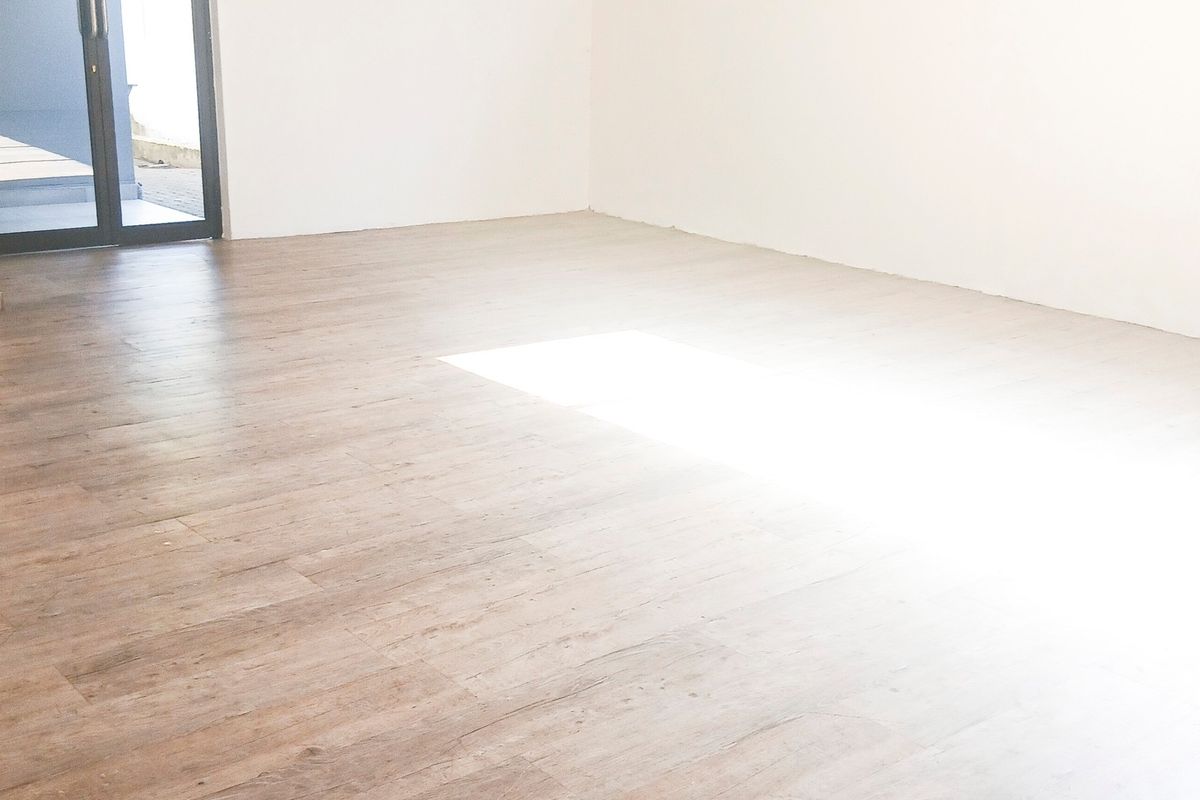 A bright, empty office space featuring modern wood-look tile flooring and a glass-paneled door leading to an outdoor area.