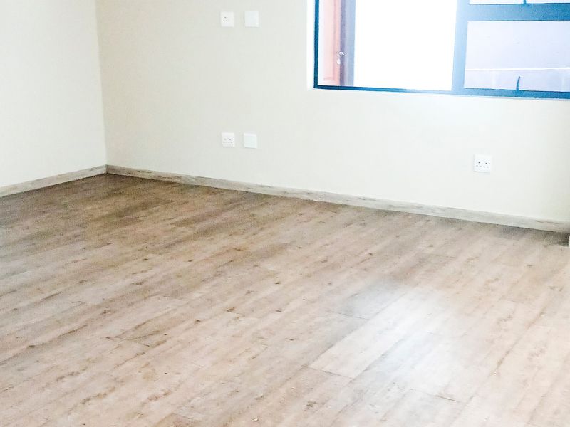 A bright, empty office space featuring modern laminate flooring, neutral walls, and an aluminium-framed window, providing a clean canvas for a professional workspace.