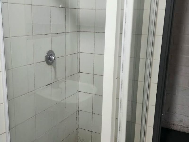 A compact shower stall featuring white wall tiles and a standard shower mixer, requiring maintenance to the grout and frame.
