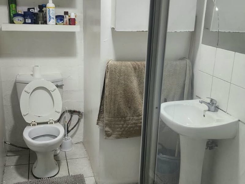 Compact bathroom featuring a pedestal basin, toilet, and shower enclosure with tiled flooring and wall-mounted storage.