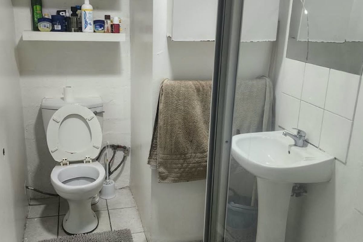 Compact bathroom featuring a pedestal basin, toilet, and shower enclosure with tiled flooring and wall-mounted storage.