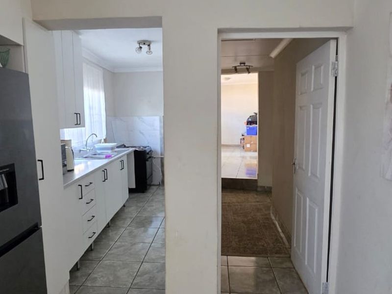 A functional kitchen featuring white cabinetry, tiled flooring, and integrated cooking appliances, with a clear view through to the adjacent living area.