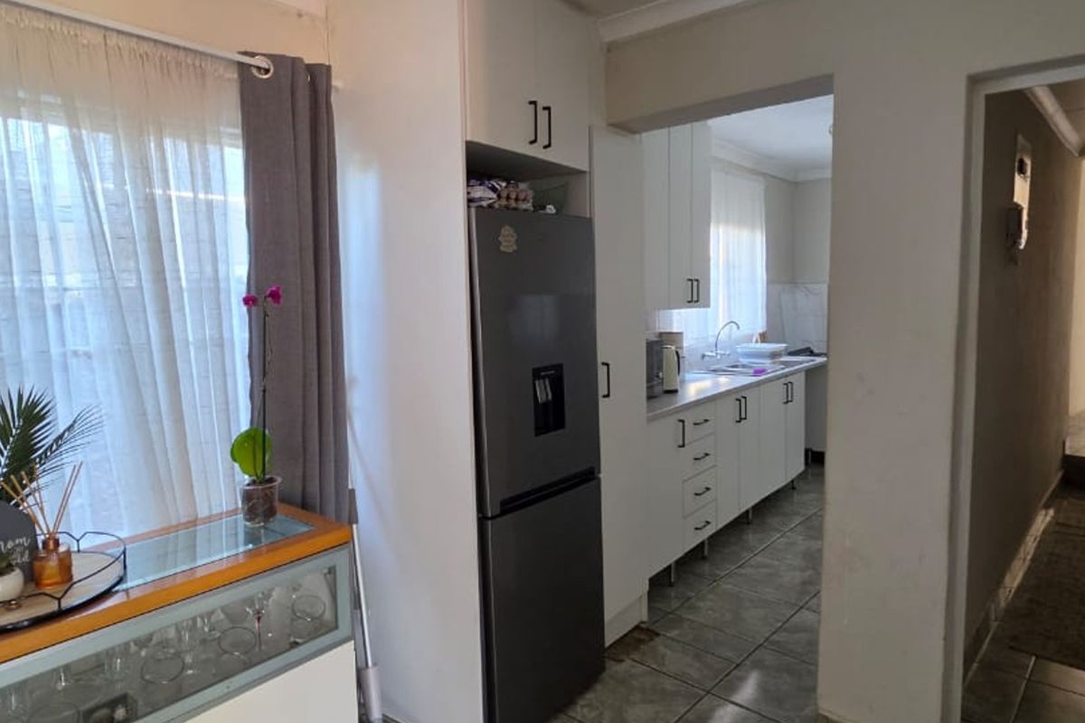 A functional kitchen area featuring white built-in cabinetry, tiled flooring, and a sink, with an adjacent view into the hallway.