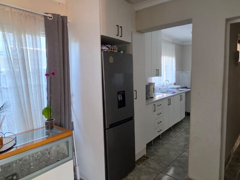 A functional kitchen area featuring white built-in cabinetry, tiled flooring, and a sink, with an adjacent view into the hallway.