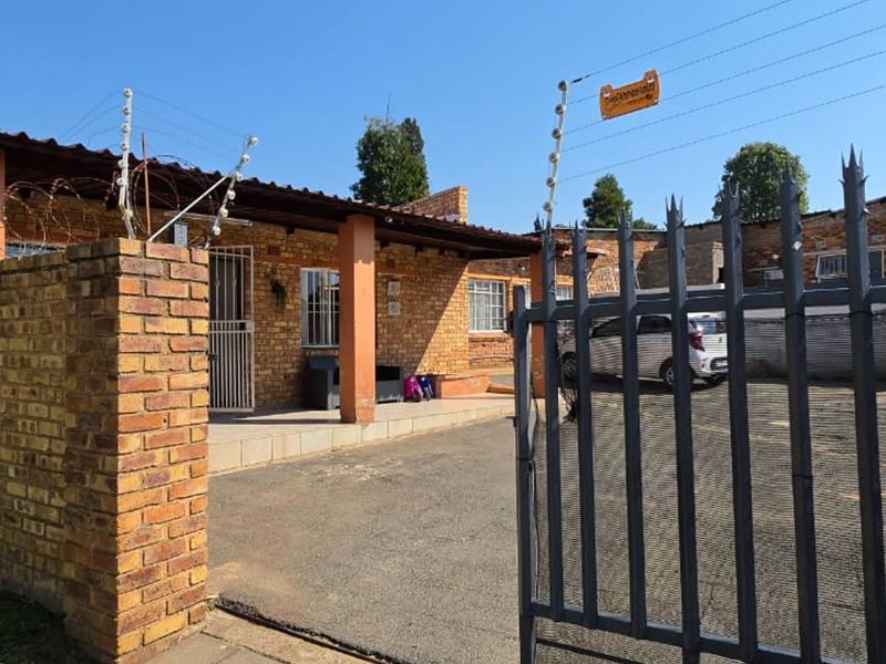 Front exterior view of a face brick cottage featuring a covered patio, paved driveway, and security fencing.
