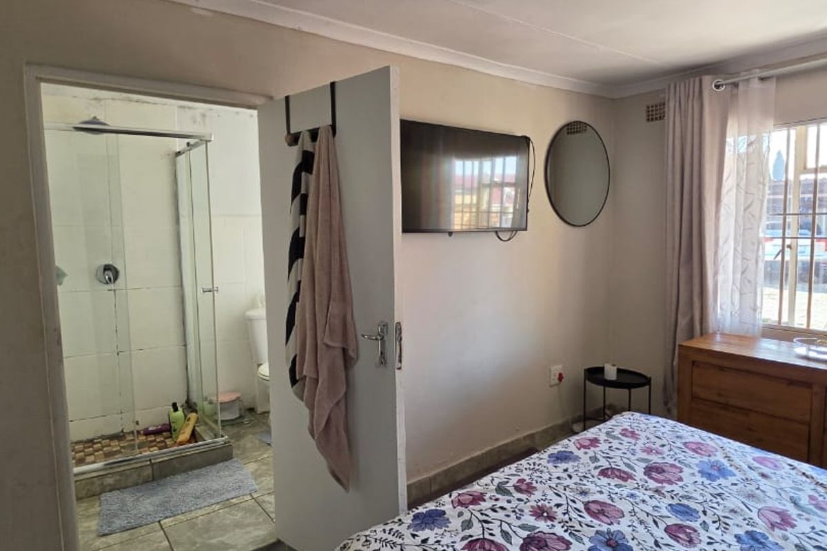 A bedroom featuring an en-suite bathroom with a glass shower enclosure, tiled flooring, and a window with security bars.
