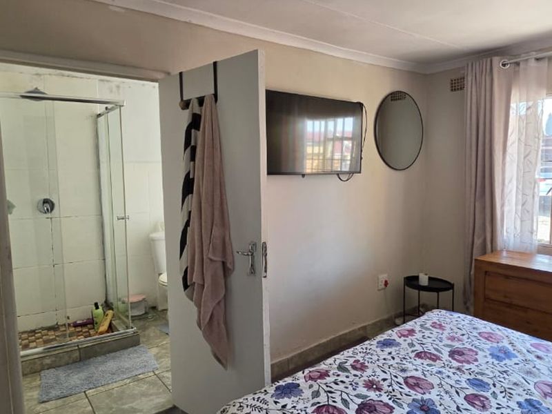A bedroom featuring an en-suite bathroom with a glass shower enclosure, tiled flooring, and a window with security bars.