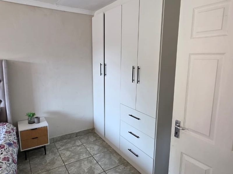 A bedroom featuring neutral walls, tiled flooring, and a modern white built-in wardrobe with integrated drawers.