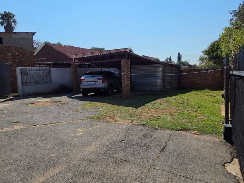 Rear exterior area featuring a covered carport, asphalt driveway, and brick boundary wall with security fencing.