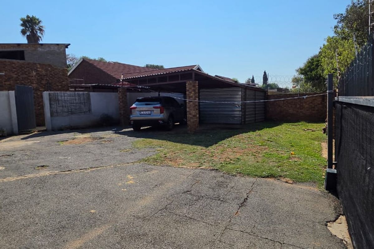Rear exterior area featuring a covered carport, asphalt driveway, and brick boundary wall with security fencing.