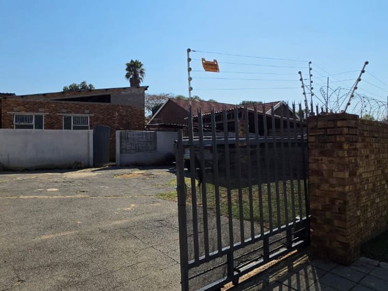 Front exterior view of the property featuring a paved driveway, secure metal gate, and brick boundary wall with electric fencing.