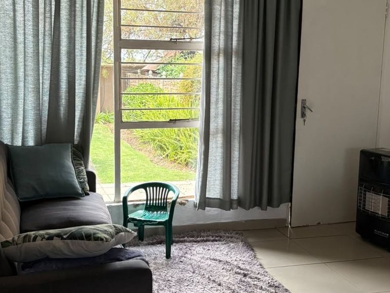 A living room featuring tiled flooring and a large window with security bars, providing natural light and a view of the garden.