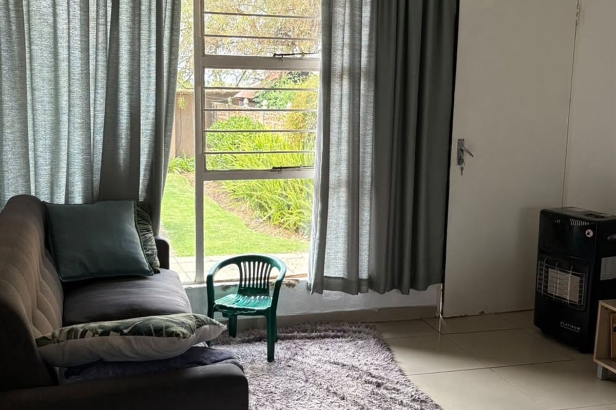 A living room featuring tiled flooring and a large window with security bars, providing natural light and a view of the garden.
