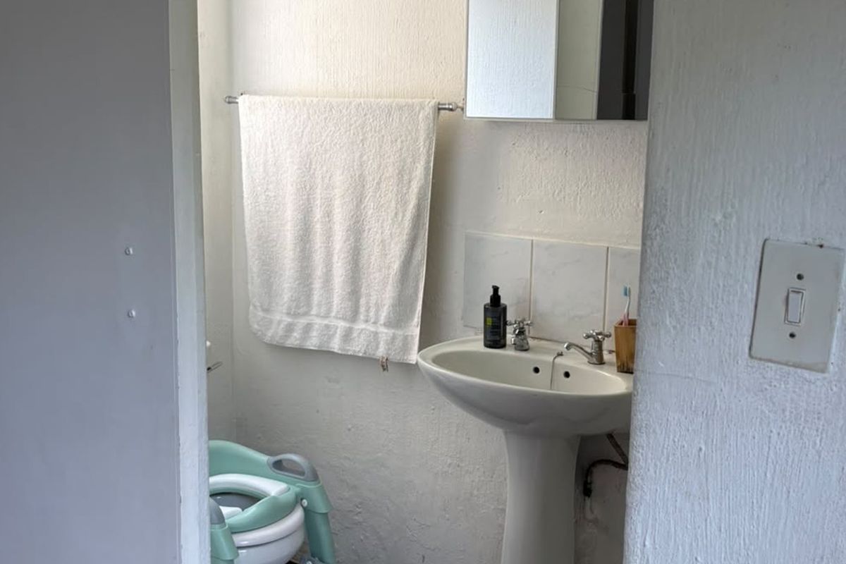 A compact bathroom featuring a pedestal basin, tiled splashback, and wall-mounted medicine cabinet, requiring cosmetic updates to the wall finishes.